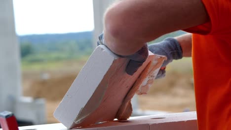 Building-a-house,-a-worker-applies-mortar-to-a-brick