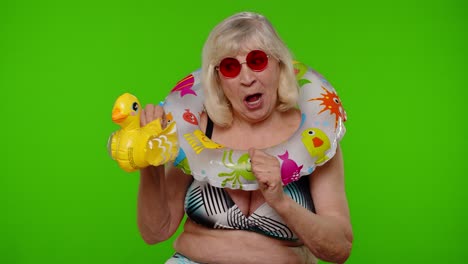 senior woman tourist in swimsuit dancing, celebrating, playing with inflatable duck toy, rubber ring