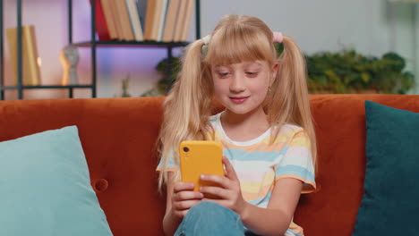 young girl smiling and looking at her phone while sitting on a couch.