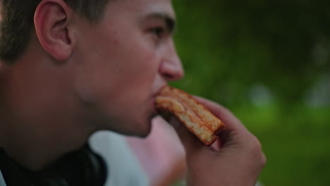 vista parcial de primer plano de un hombre comiendo un sándwich a la parrilla con un fondo ligeramente borroso de la persona comiendo, al aire libre, entorno natural con iluminación suave