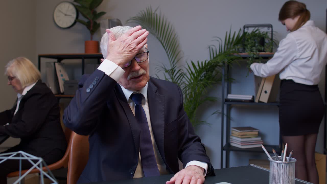 Kedsommelig ældre mandlig chef slår sig i panden, mens han udvikler et nyt projekt på sin bærbare computer.