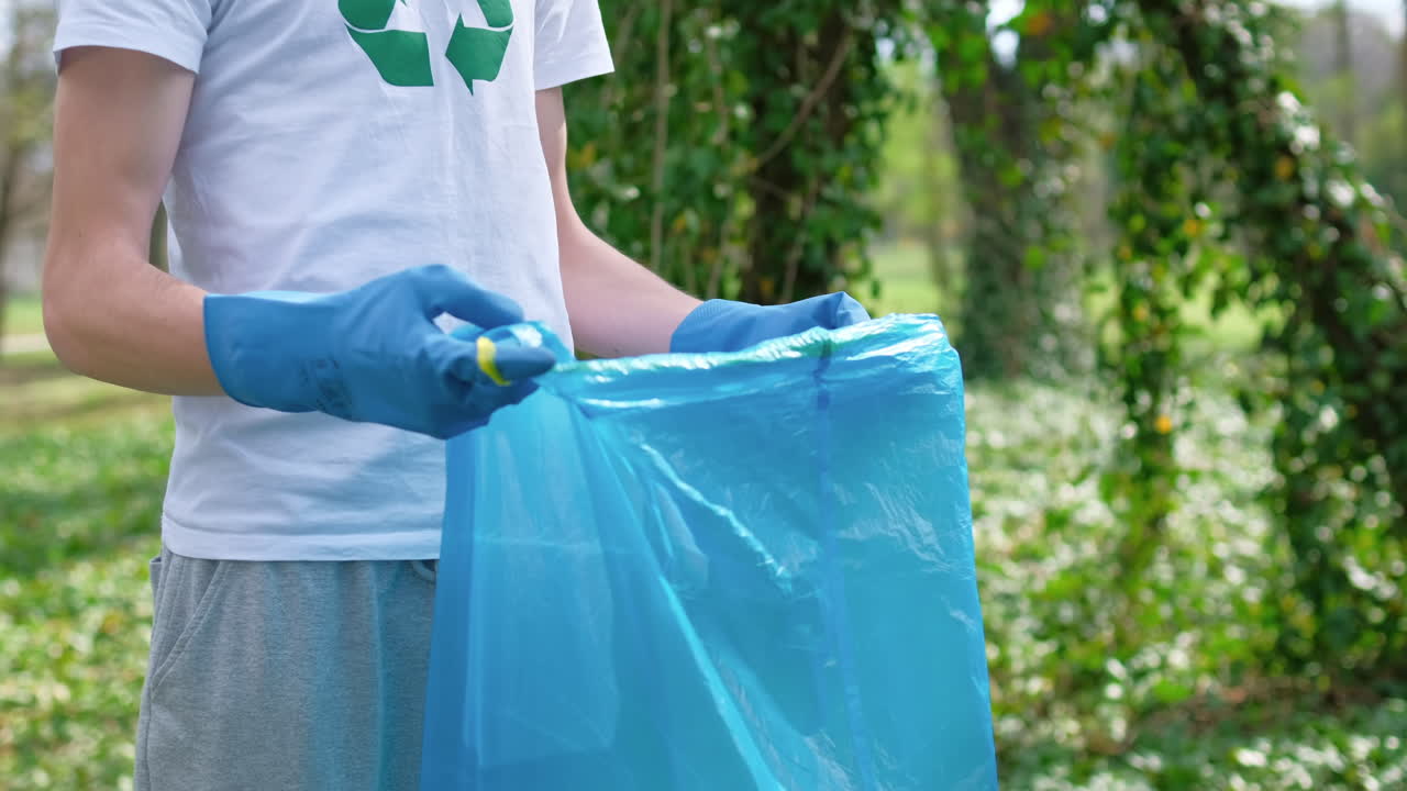Two men collecting plastic garbage in bag in a polluted park. Rubber gloves, recycling sign on T-shirt