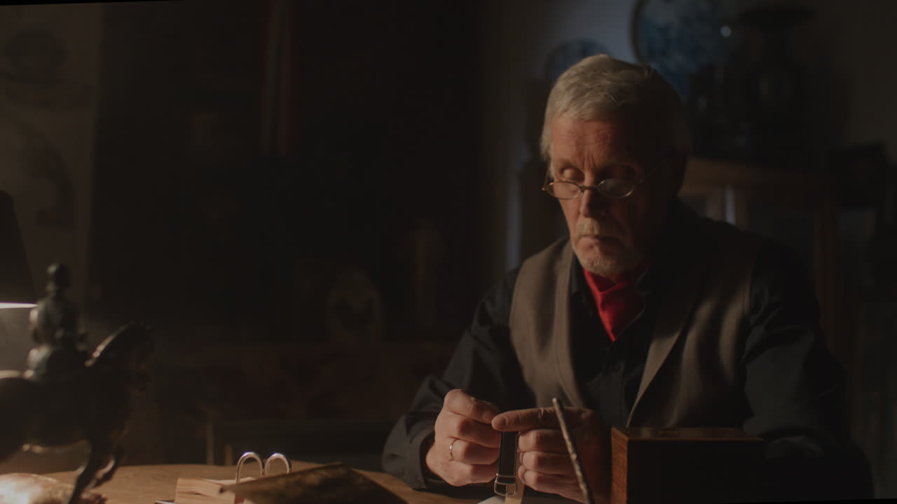 Older passionate man evaluates an old watch in his office at night