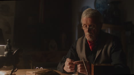 older passionate man evaluates an old watch in his office at night