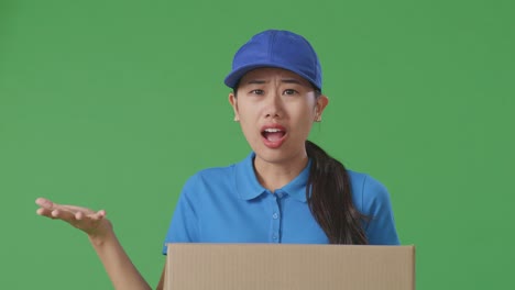 primer plano de una mensajera asiática en uniforme azul mostrando un gesto desconcertado y diciendo qué mientras entregaba una caja de cartón en el fondo de la pantalla verde en el estudio