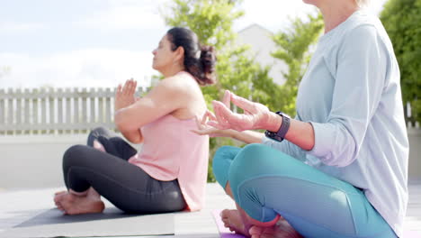 Zwei-Glückliche,-Vielfältige-Seniorinnen-Praktizieren-Yoga-Im-Sonnigen-Garten,-Zeitlupe