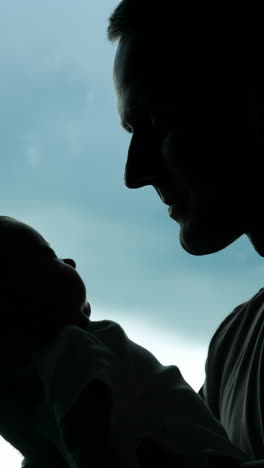 silhouette of a man holding a little baby. loving father kissing his adorable child. window at backdrop. vertical video