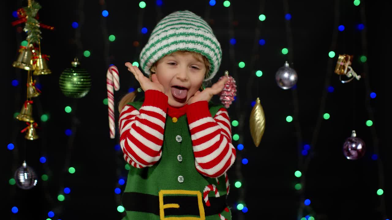 Holčička v kostýmu vánočního skřítka, pomocníka Santa Clause, si zakrývá obličej rukama a hraje si na schovávanou.