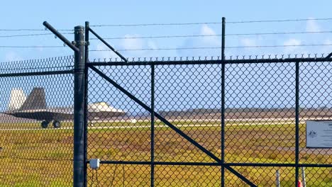 an f-22 raptor taxis on a runway behind a fence at avalon airshow, geelong, under clear skies