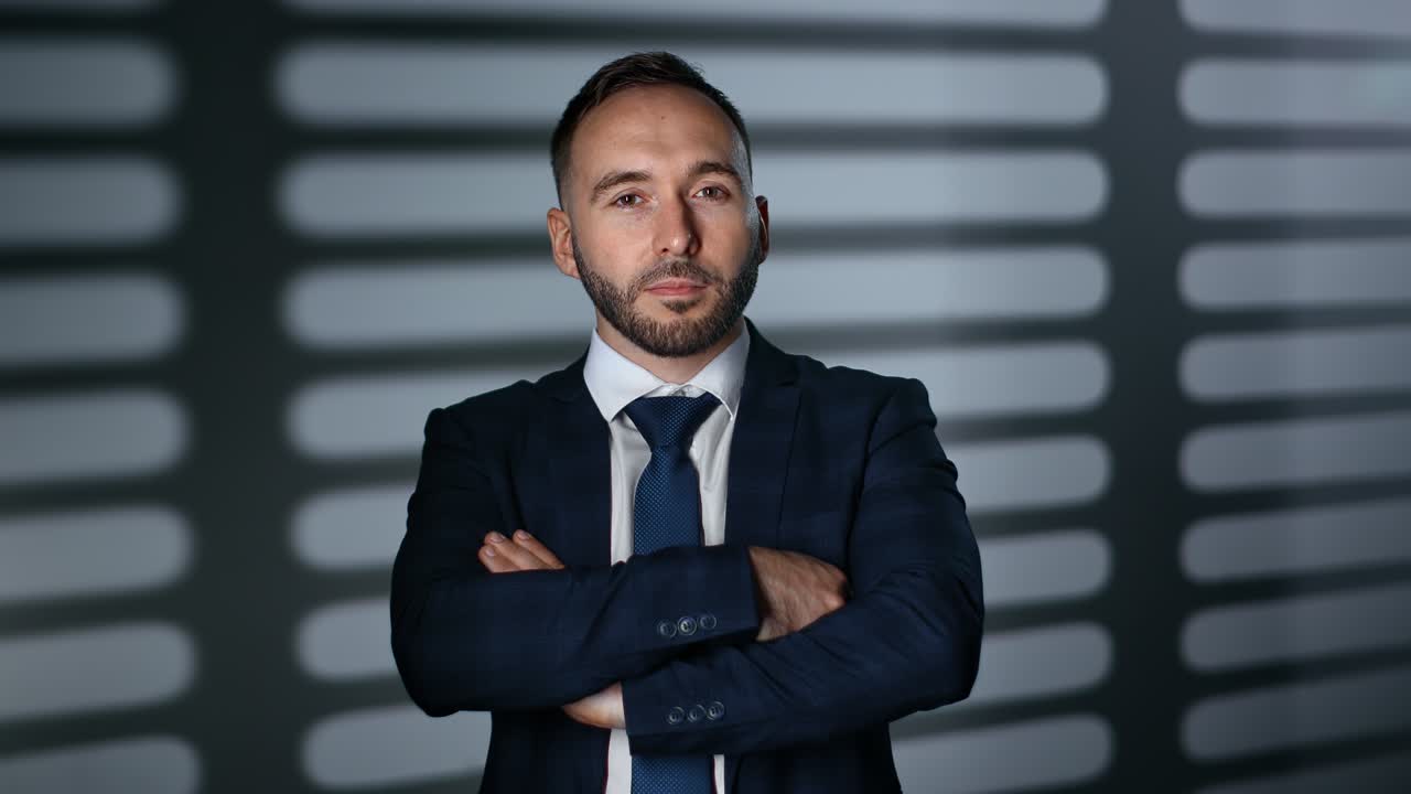 hombre de negocios guapo traje de moda corbata posando con las manos cruzadas en la oficina de la noche con la sombra de los celos