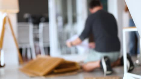 a man kneels on the floor assembling wooden furniture in a bright, modern living room with soft lighting