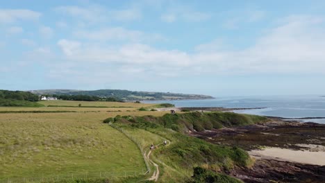 Hikers-trekking-Traeth-Lligwy-Anglesey-eroded-coastal-shoreline-aerial-view-reversing-over-Welsh-weathered-coastline