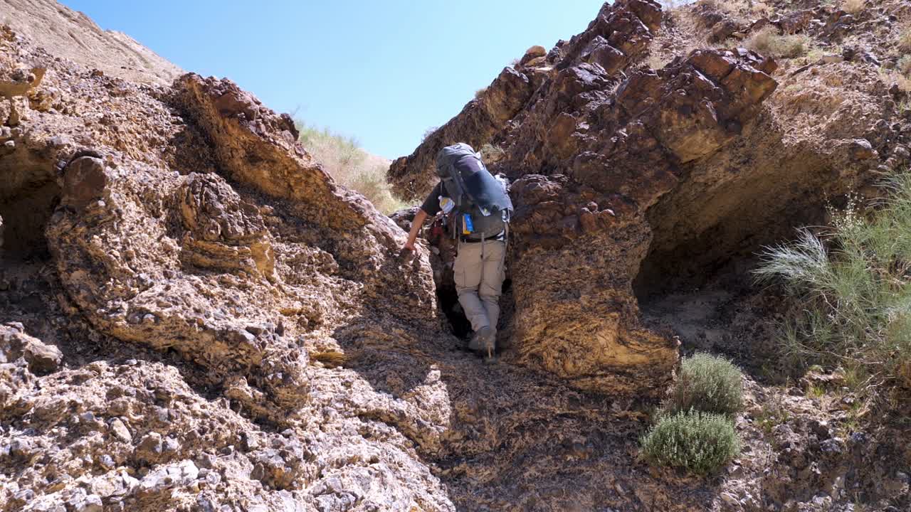 excursionista macho adulto escalando cuidadosamente una pequeña pared de roca con una mochila grande en el sendero del cráter ramon en israel