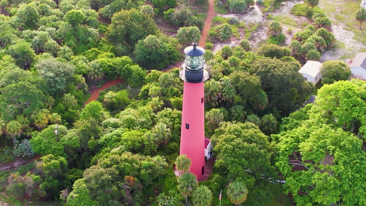 A stunning aerial shot of a tall, red lighthouse surrounded by dense, vibrant green forest