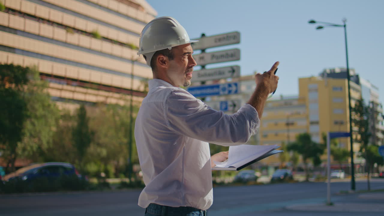 Hardhat architect talking instructions remotely at summer city street closeup