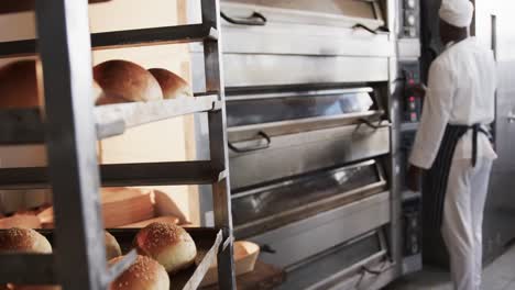 african american male baker working in bakery kitchen, checking oven in slow motion