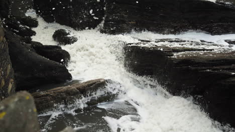 white sea foam washed ashore and blown by the wind onto the rocks at ilfracombe, north devon coast, england, united kingdom