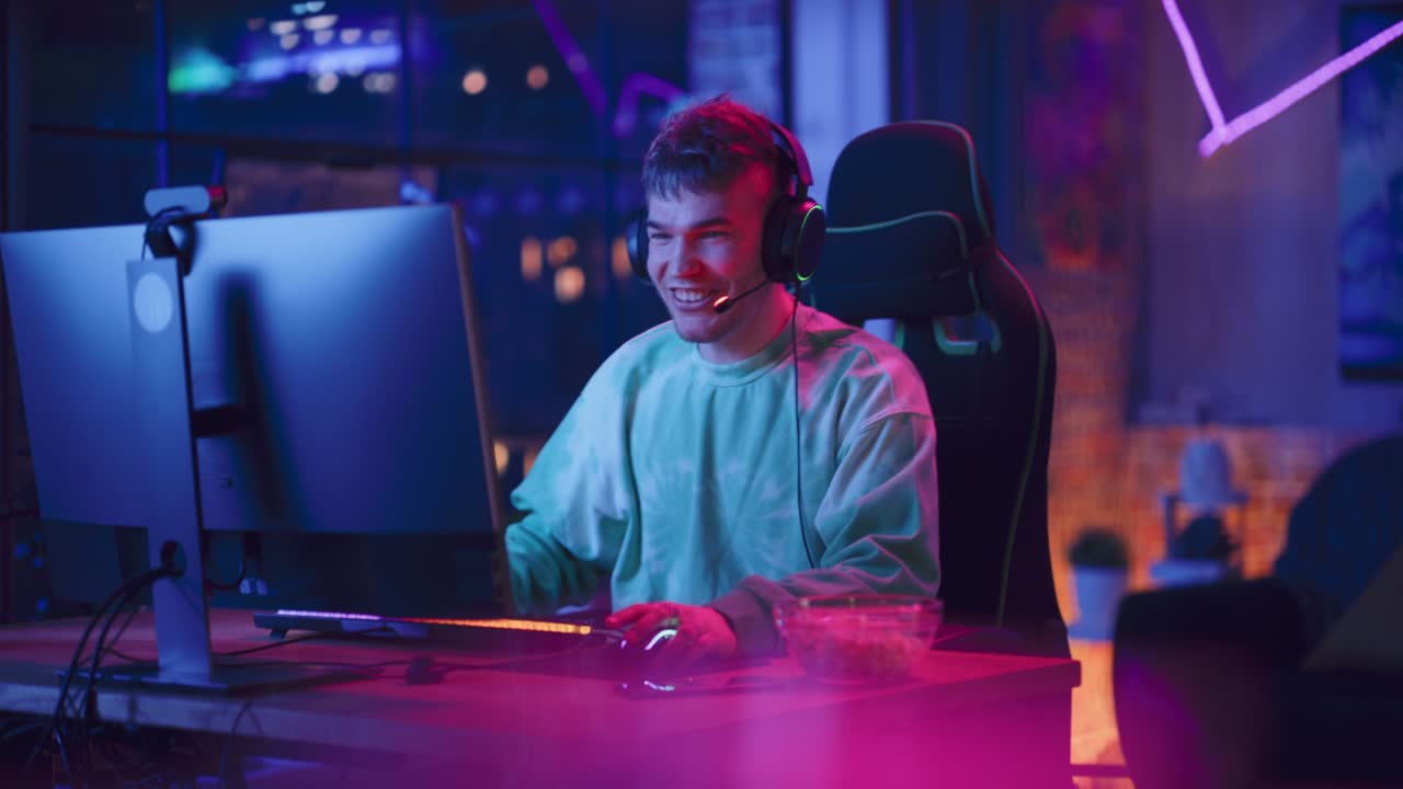 Gamer di successo che vince in un videogioco online al computer. Ritratto di giovane uomo elegante con le cuffie che gioca a un torneo PvP con altri giocatori e parla con la squadra al microfono.
