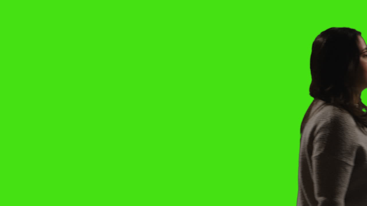 mujer joven con gafas caminando a través del cuadro contra el fondo de la pantalla verde con iluminación de baja clave 1