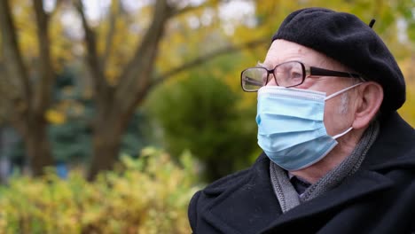 a senior man in a medical protective mask and goggles is resting in the park. covid health and safety concept, coronavirus quarantine.