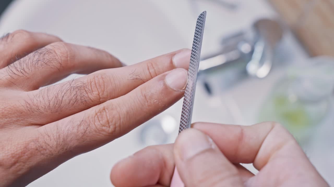 Close-up of a man's hands while he files his fingernails with an emery board. Male personal hygiene and grooming routine in the bathroom