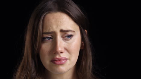 studio shot of unhappy young woman crying into camera