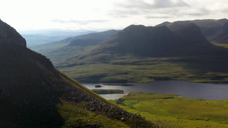 rotating drone shot of stac pollaidh in the northwest highlands of scotland, passing over rocky mountain tops to with bodies of water in the distance