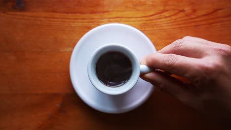 hand is serving hot espresso cup on a white plate, standing on a brown wooden table