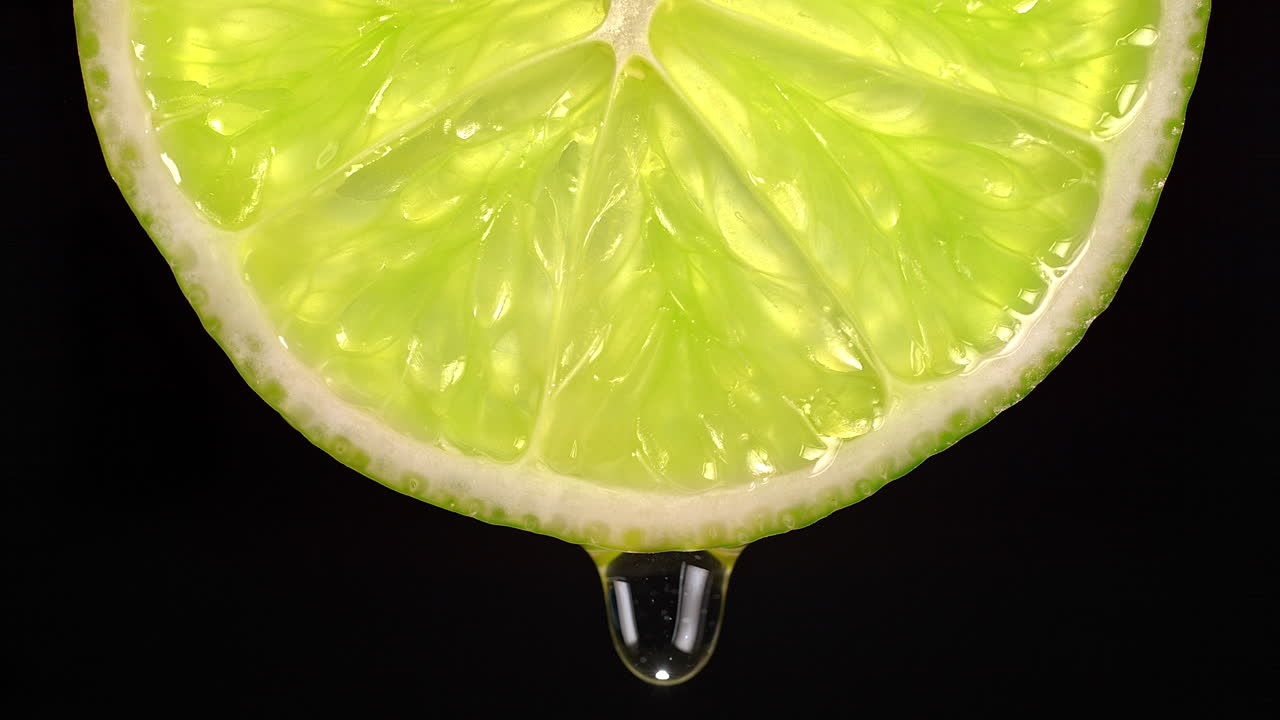 gotas de agua que gotean de una rodaja de cal en cámara lenta sobre un fondo negro