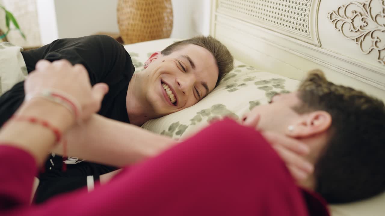 To unge menn som ler og snakker i sengen.