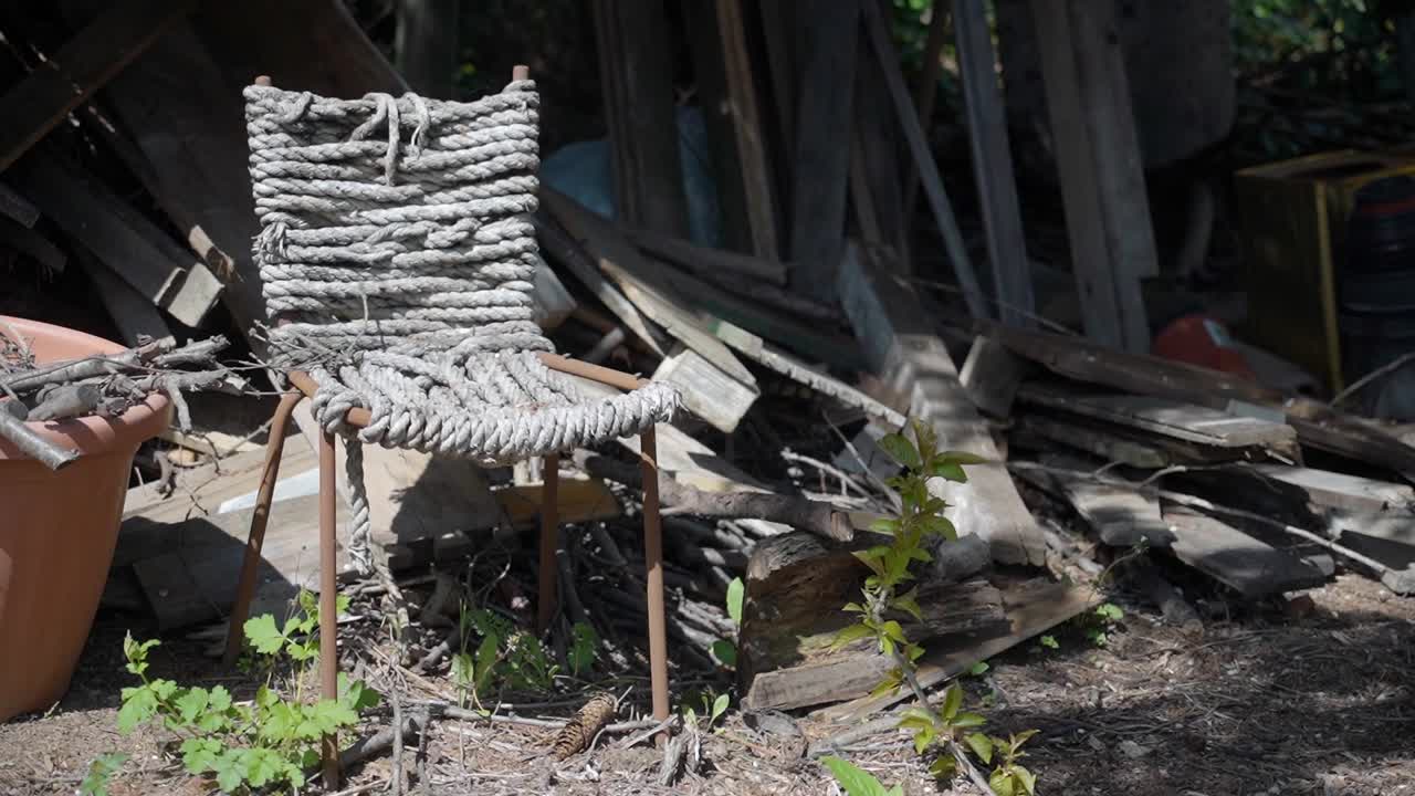 Worn rope chair placed near a garden shed with wooden debris