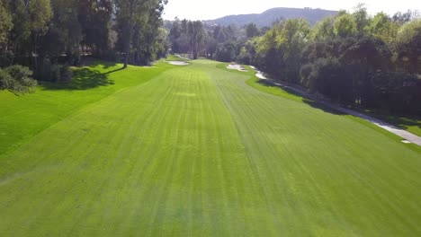 4k aerial drone view of calabasas country club in los angeles, california with lush fairways and white sand bunkers on a warm, sunny day