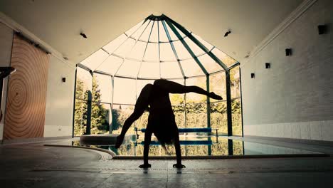 Gimnasta-Femenina-Haciendo-Parada-De-Manos-Y-Movimiento-De-Piernas-Junto-A-La-Piscina-Cubierta,-Silueta