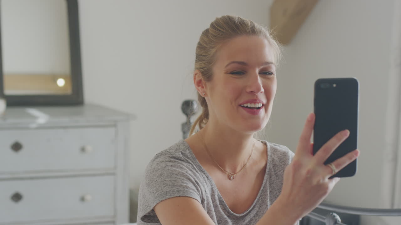 mujer con teléfono móvil vistiendo pijama teniendo chat de video sentada en la cama