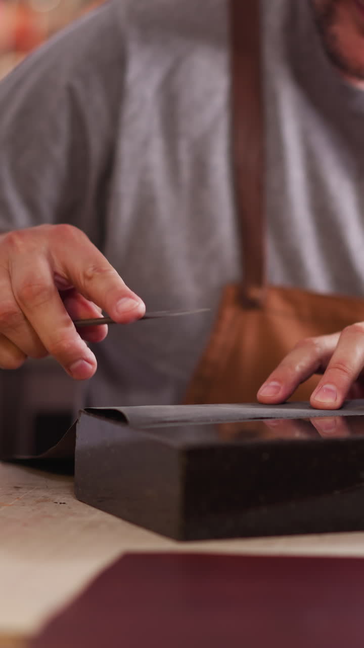 Craftsman sharpens cutter with sandpaper at table in shop closeup. Leathersmith processes tool for work in studio. Worker with knife at workplace