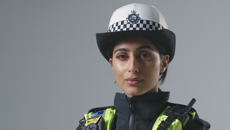 Studio-Portrait-Of-Serious-Young-Female-Police-Officer-Against-Plain-Background