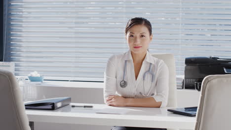 portrait of smiling female doctor with stethoscope sitting at desk in office