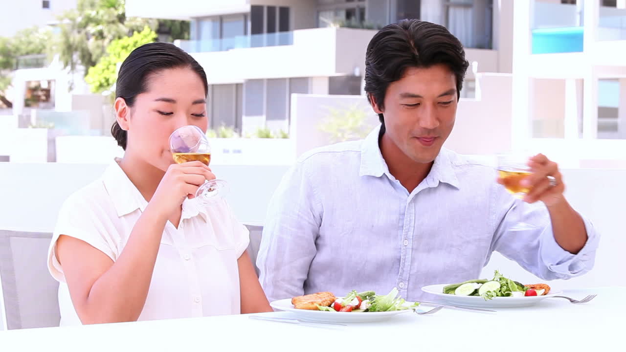 una pareja asiática tomando vino blanco con su comida.
