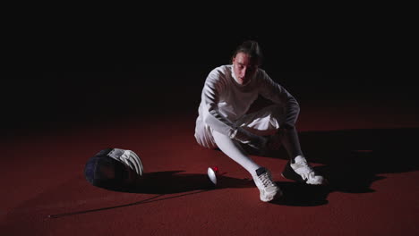 a young fencer sitting on the floor looking disappointed after a match