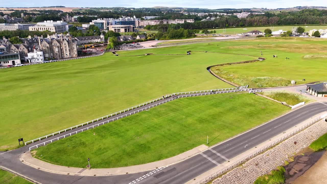 Drone footage glides above the Old Course at St Andrews, revealing manicured greens, Victorian architecture, and coastal roads in bright daylight