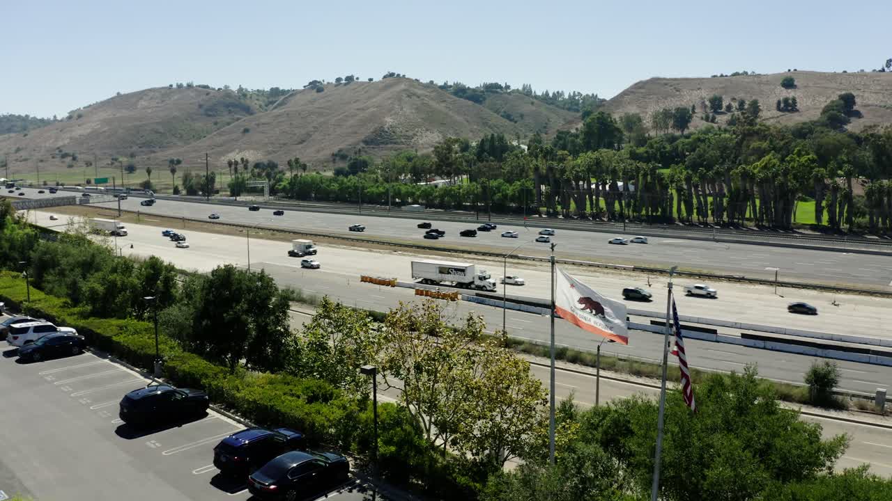 Drone shot approaching a freeway with the California State Flag waving in the foreground.