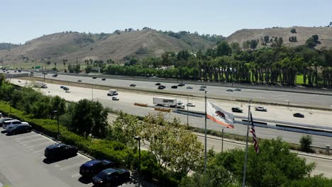 drone shot approaching a freeway with the california state flag waving in the foreground.
