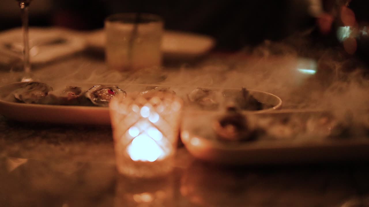 A cozy, candlelit setting with oysters and drinks on a table. Warm lighting creates an intimate dining atmosphere