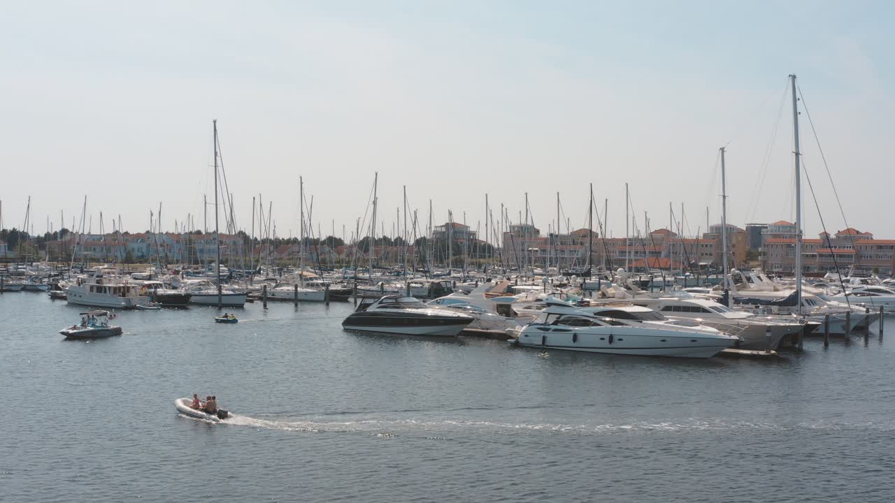 Cinematic drone - aerial shot of three boats on a marina in the background with sailing boats on a sunny day, 25p