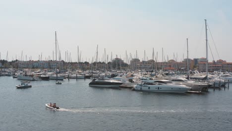 Cinematic-drone---aerial-shot-of-three-boats-on-a-marina-in-the-background-with-sailing-boats-on-a-sunny-day,-25p