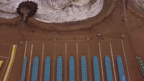 aerial top down of colorful tents of spa resort at sandy beside crashing waves of ocean - mar del plata,argentina - ascending drone shot