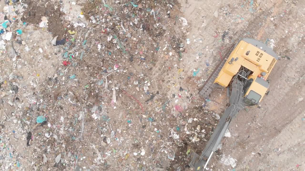 excavador limpiando basura apilada en un vertedero lleno de basura