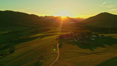 Puesta-De-Sol-Sobre-Una-Aldea-Rural-Cerca-Del-Lago-Attersee-Con-El-Sol-Asomándose-Sobre-La-Vista-Aérea-De-Las-Montañas