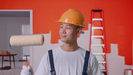 primer plano de un pintor asiático con casco de seguridad pintando y sonriendo con la pared de la pintura en la habitación