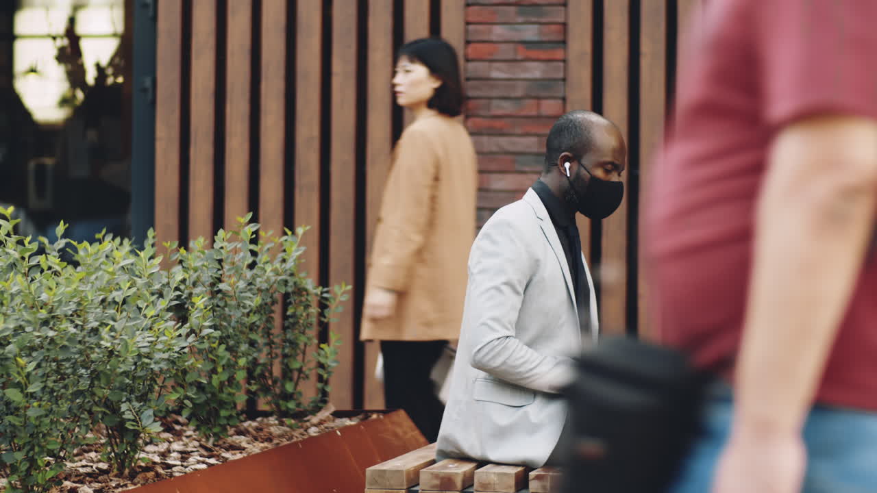 Accéléré d'un homme d'affaires noir masqué travaillant sur un ordinateur portable sur un banc public